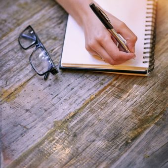 Cropped shot of a woman sitting at a table and writing in her notepad.